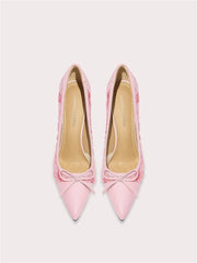 Pair of pink high-heeled shoes with bow details on a light gray background