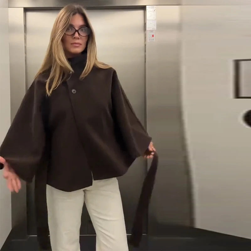 Woman in a brown coat and white pants standing in an elevator.
