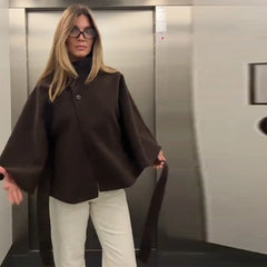 Woman in a brown coat and white pants standing in an elevator.