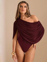 Woman wearing a burgundy one-shoulder swimsuit on a beige background