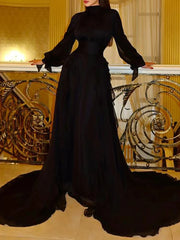 Woman in a long black evening gown standing in an elegant interior setting.