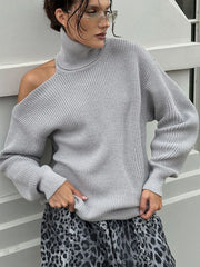 Person wearing a gray sweater with one shoulder exposed, standing against a white railing.