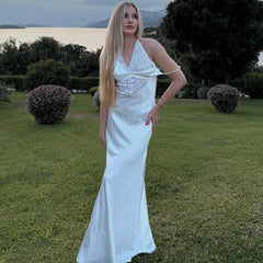 Woman in a white dress standing outdoors with greenery and water in the background