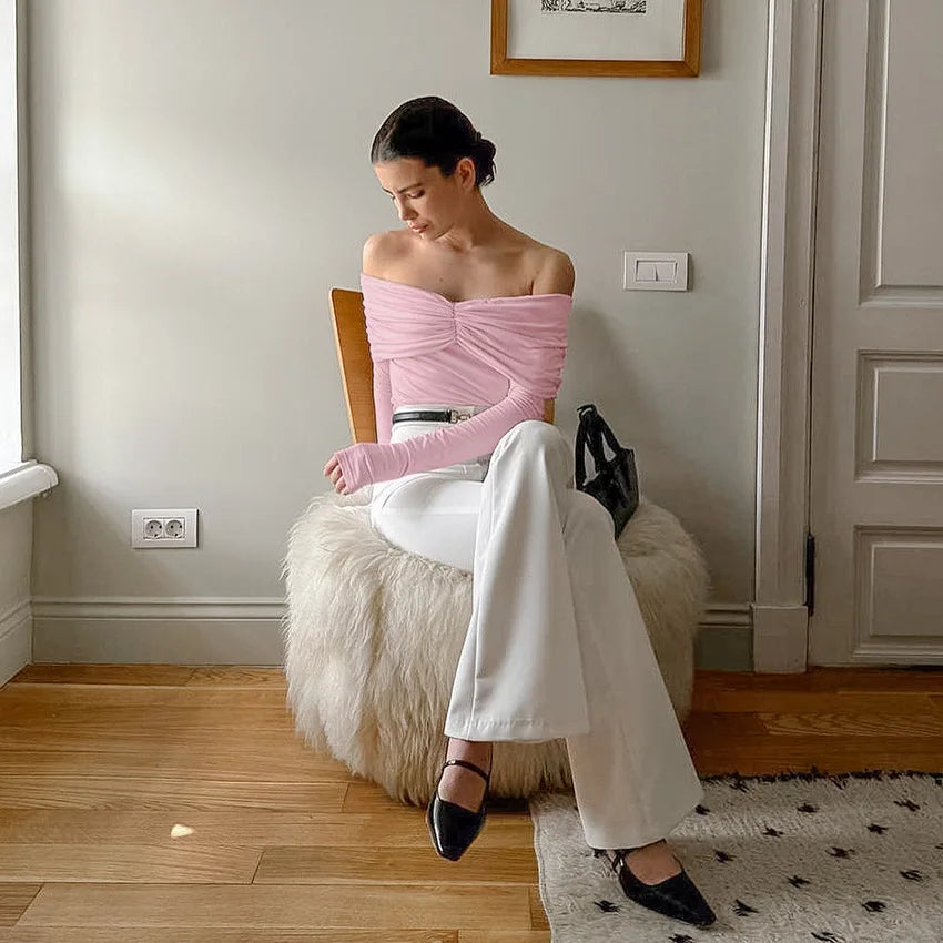 Woman sitting on a fluffy chair wearing a pink top and white pants in a room with wooden flooring and a door.