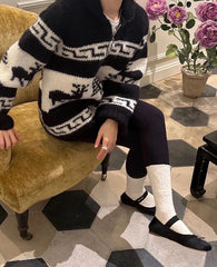 Person wearing a patterned sweater sitting on a chair with a decorative rug and flowers in the background.