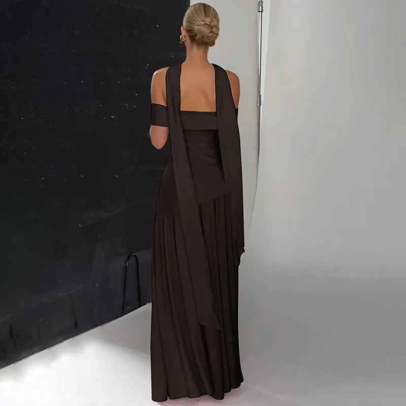 Woman wearing a long brown dress standing against a black backdrop in a studio setting.