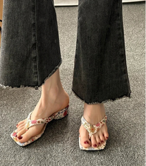Floral sandals worn with black jeans on a gray floor.