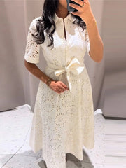 Woman wearing a white lace dress with a bow tie in a minimal indoor setting.