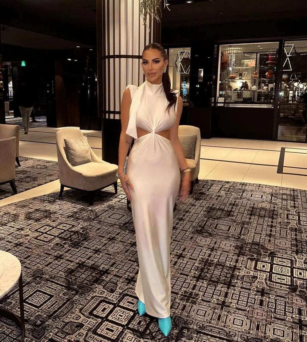 Woman in a white dress standing in a stylishly decorated room with patterned carpet and modern furniture.