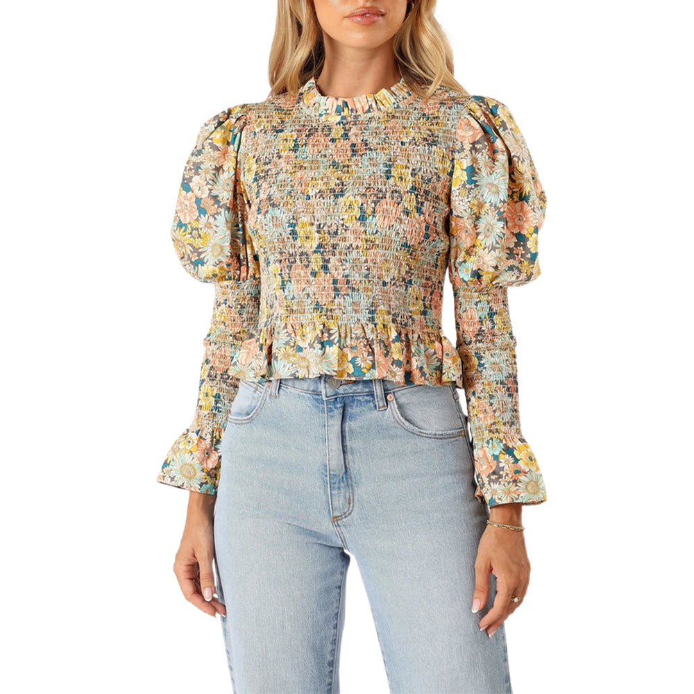 Woman wearing a floral blouse with puffed sleeves and light blue jeans on a white background