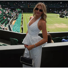 Woman in a white polka dot dress standing on a tennis court with spectators in the background