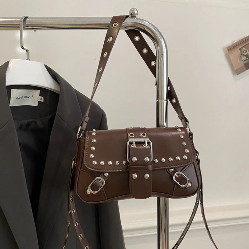 Brown studded handbag hanging on a rack with a black blazer and white shirt in the background.
