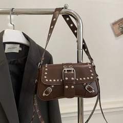Brown studded handbag hanging on a rack with a black blazer and white shirt in the background.