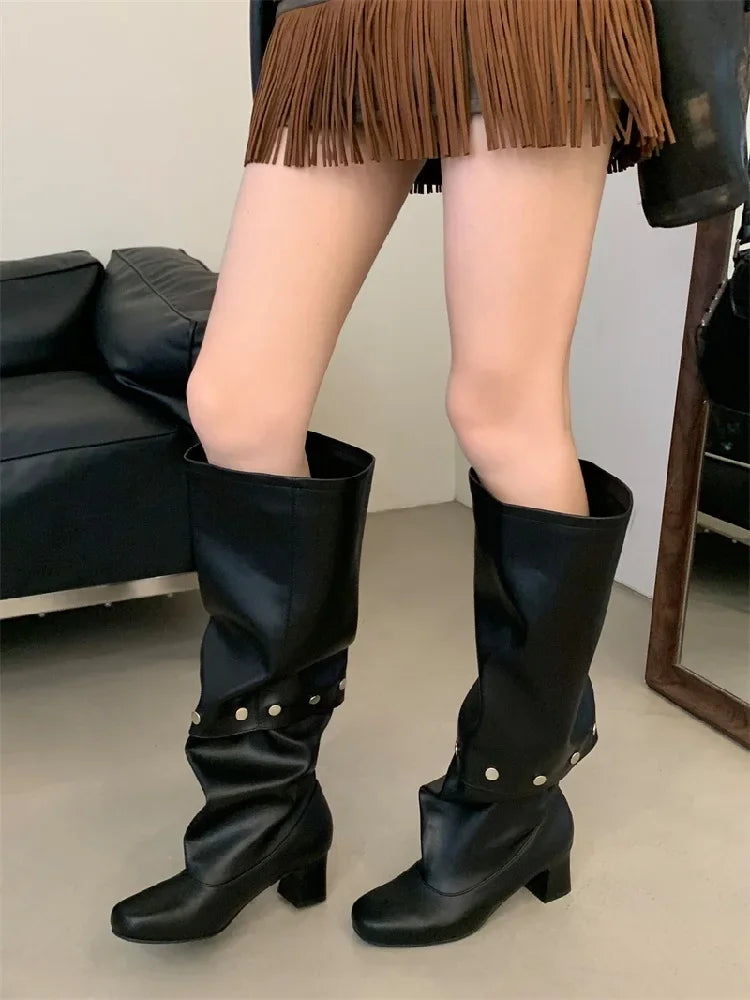 Black knee-high boots with gold studs worn by a person in a room.