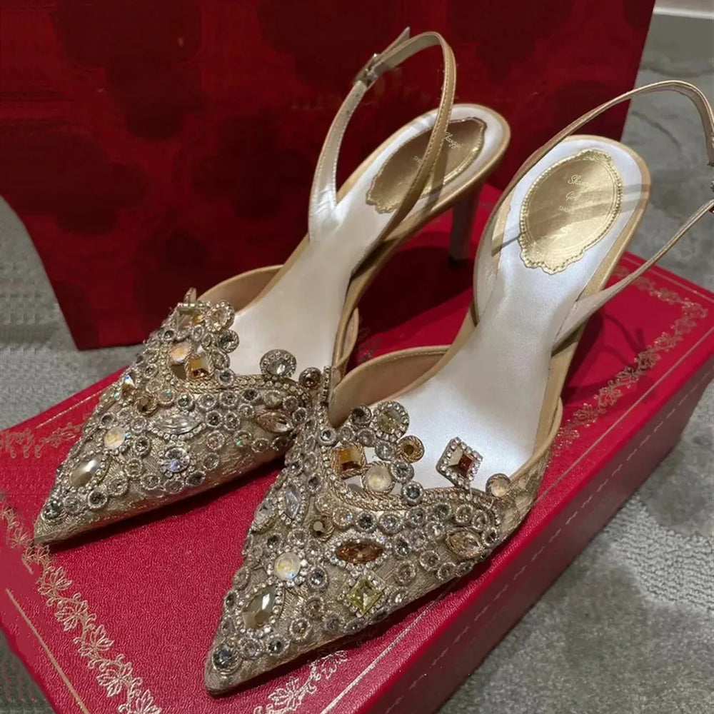 Pair of embellished high-heeled shoes on a red box with a textured surface.