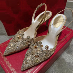 Pair of embellished high-heeled shoes on a red box with a textured surface.