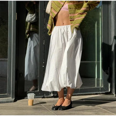 Person wearing a white skirt and green cardigan standing in front of a glass door.