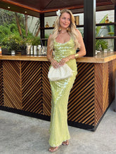 Woman in a green sequin dress holding a white clutch in front of a wooden bar.
