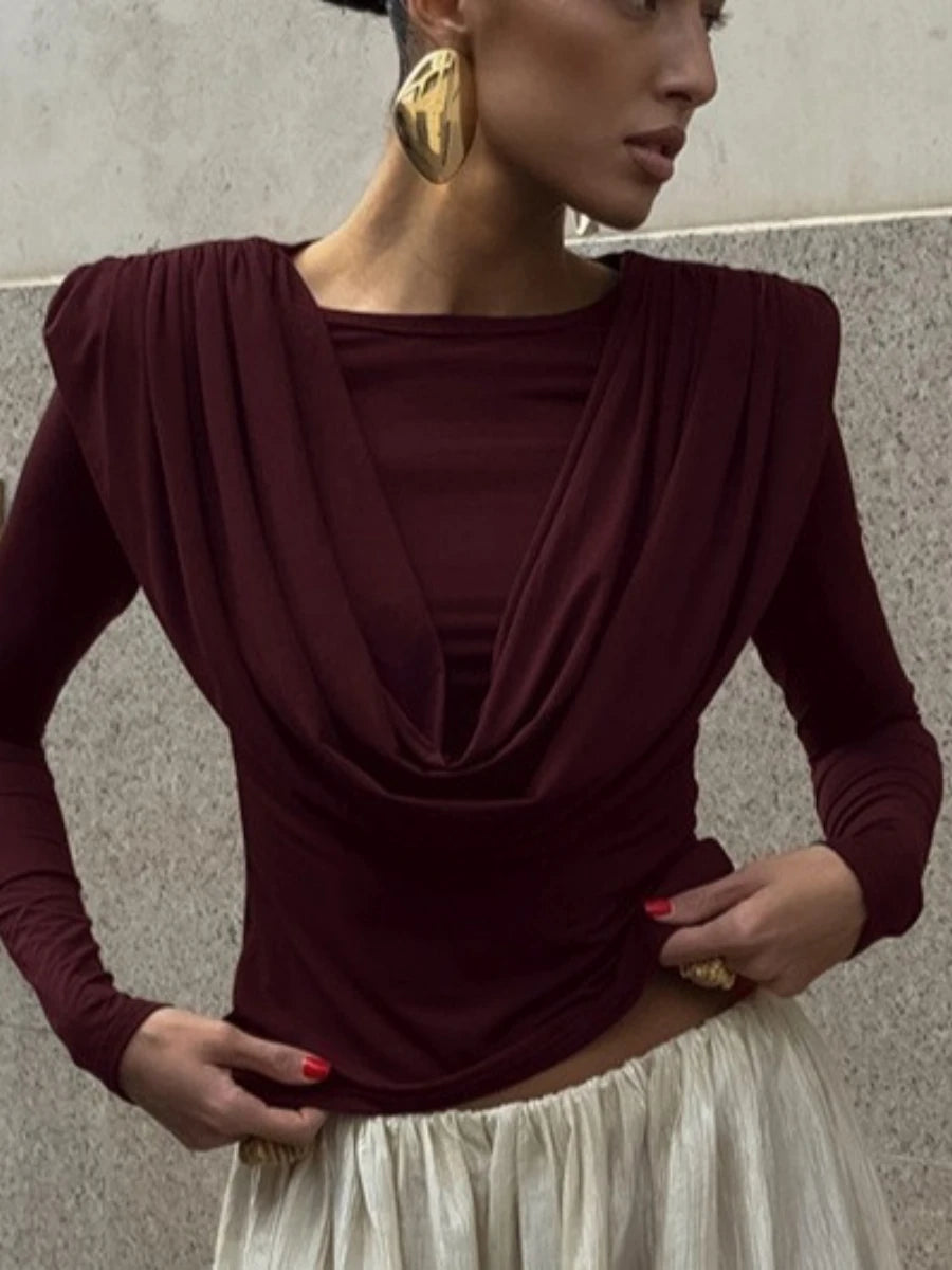 Woman wearing a burgundy long-sleeve top with a draped design against a neutral background
