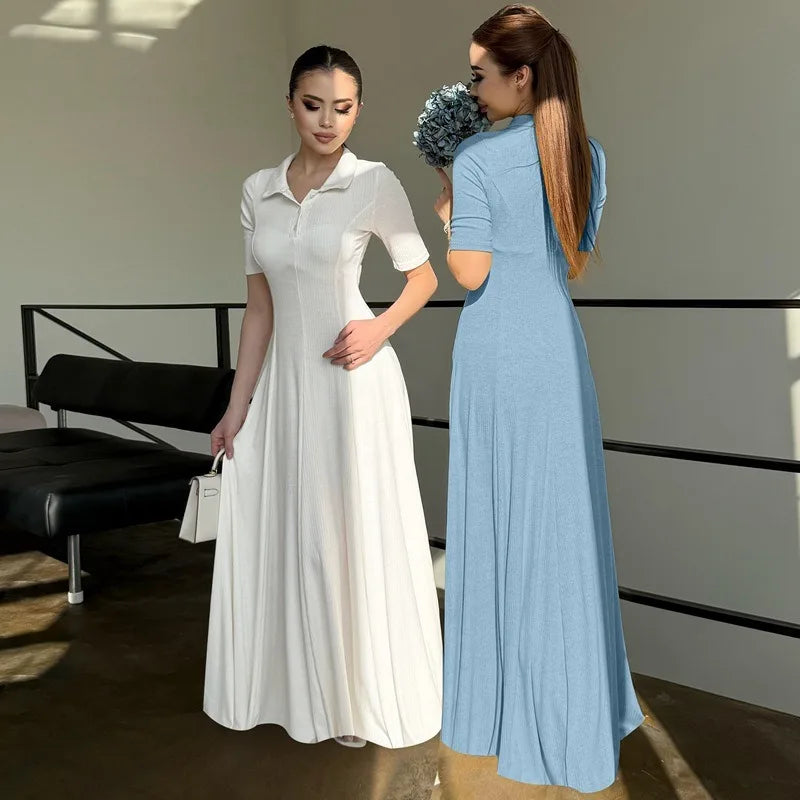 Two women in long dresses standing in a room with a black chair and white wall.