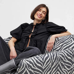 Woman in a black top sitting on a zebra-patterned sofa against a plain background