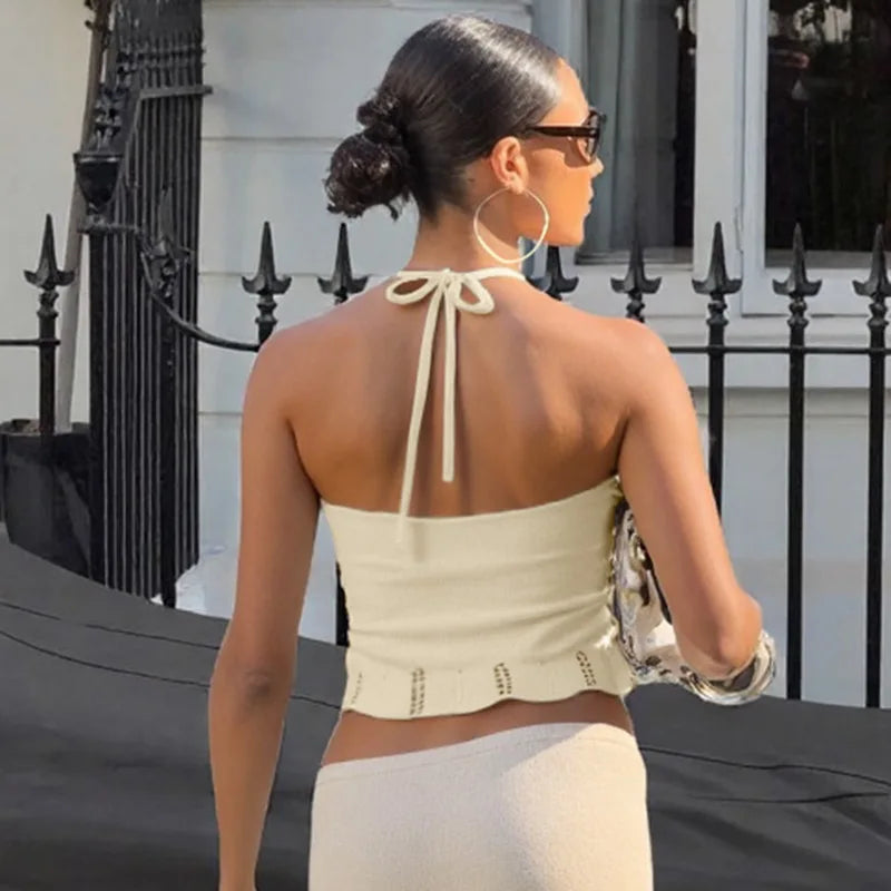 Woman wearing a beige halter top with a black metal gate and white building in the background