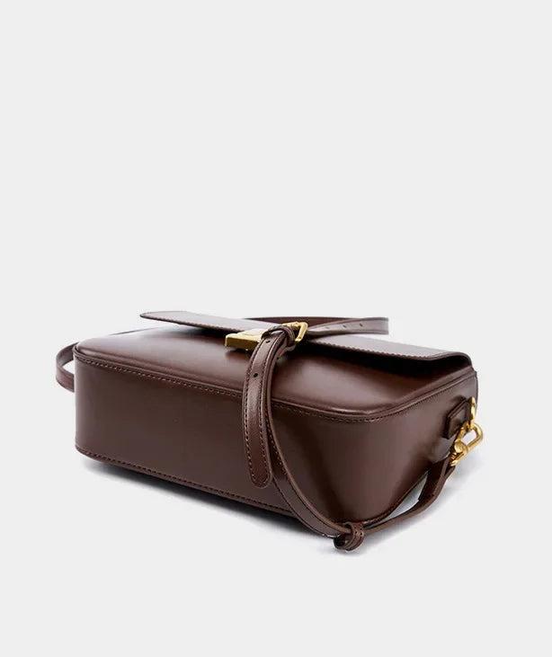 Brown leather handbag with gold accents on a light gray background