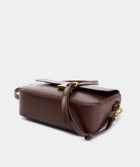 Brown leather handbag with gold accents on a light gray background