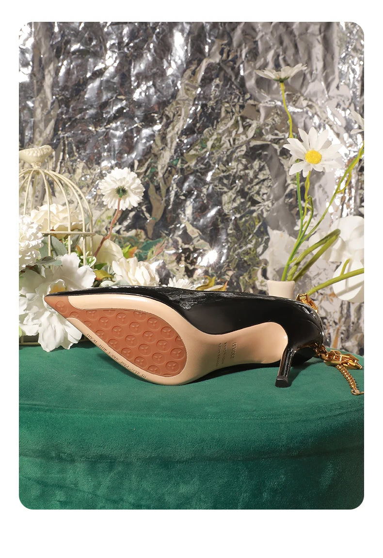 Black high-heeled shoe with beige sole on a green surface with decorative elements.