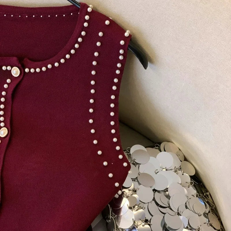 Maroon cardigan with pearl embellishments on a hanger next to silver sequin fabric.