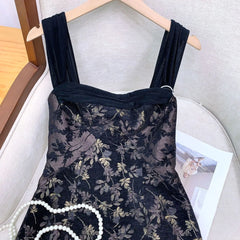 Black floral dress on a hanger with a pearl necklace beside it.