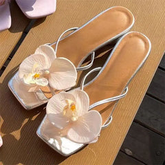Silver high-heeled sandals with white floral decorations on a wooden surface