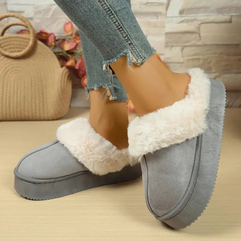 Gray slippers with white fur trim worn by a person, with a blurred background.
