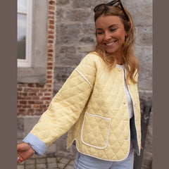 Woman wearing a light yellow quilted jacket standing against a stone wall.