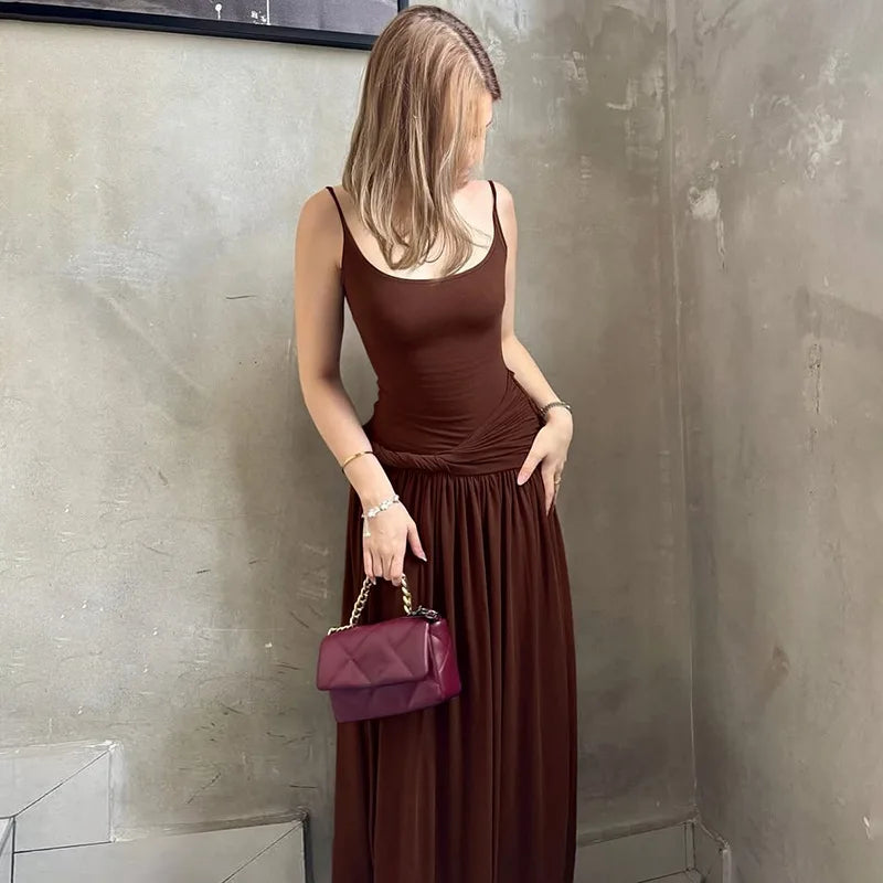 Woman in a brown dress holding a purple handbag against a textured wall.