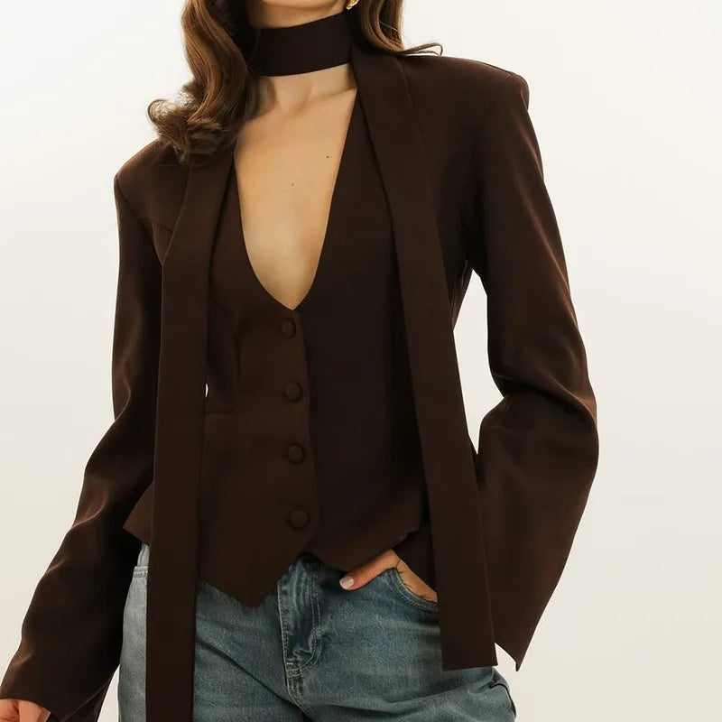 Brown blazer over a black top with blue jeans on a white background