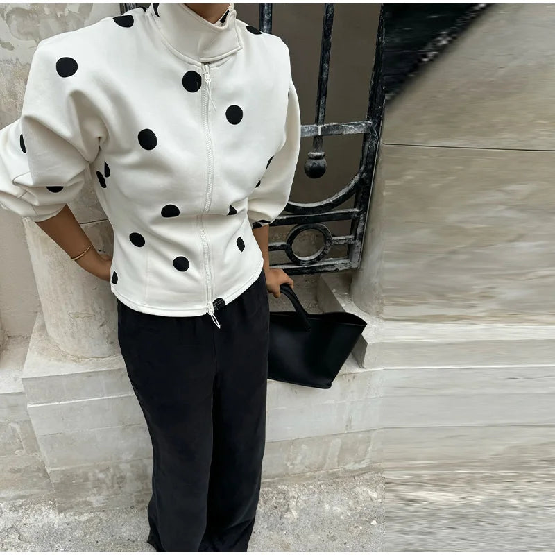 Person wearing a white jacket with black polka dots and black pants, holding a black handbag.