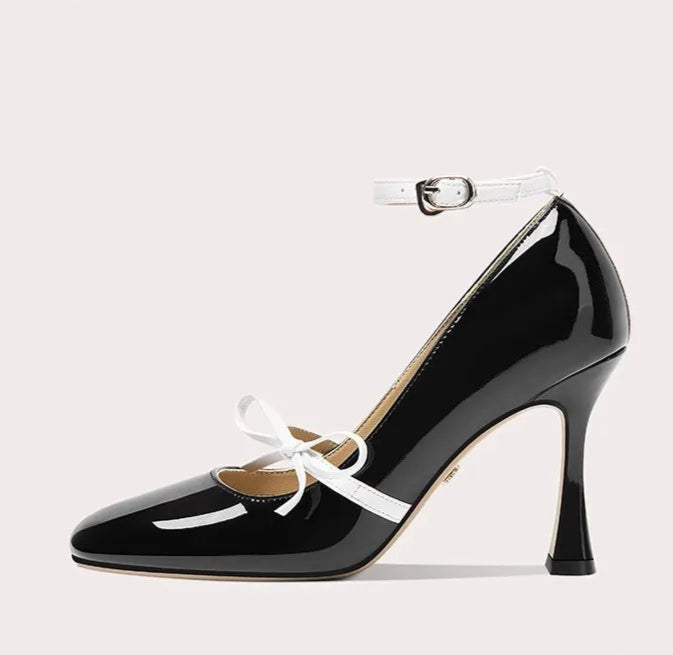 Black high-heeled shoe with white ankle strap on a light gray background