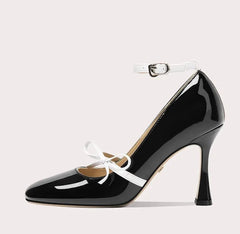 Black high-heeled shoe with white ankle strap on a light gray background