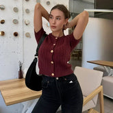 Woman in a maroon knitted cardigan and black jeans posing in a modern interior setting.