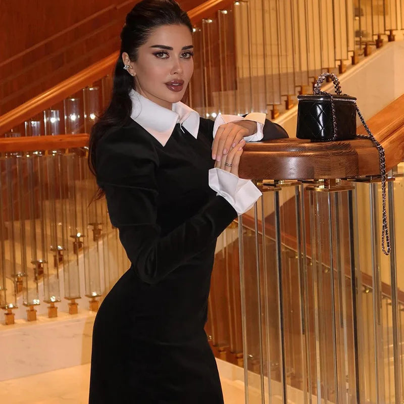 Woman in a black dress with white gloves posing next to a staircase.