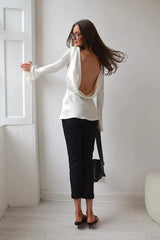 Woman wearing a white open-back top and black pants in a minimalistic room.