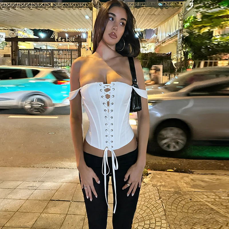 White lace up off shoulder corset top on a woman standing on a sidewalk at night.