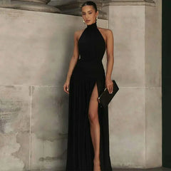 Woman in a black halter neck gown with a high slit standing against a stone wall.
