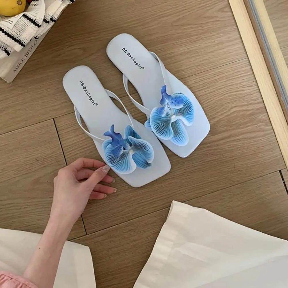 White sandals with blue flower designs on a wooden floor