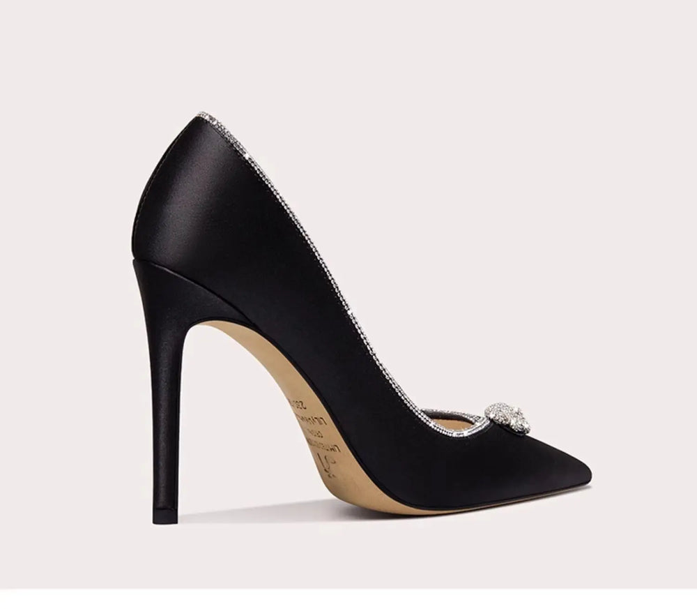 Black high-heeled shoe with a decorative brooch on a light gray background