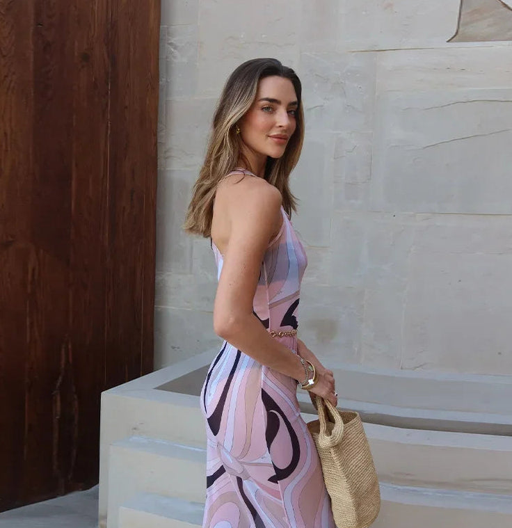 Woman in a pink dress with black abstract patterns standing on steps.