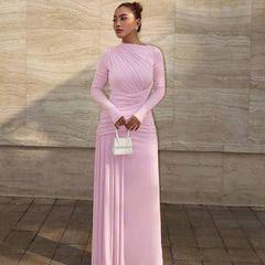 Woman in a pink dress holding a white handbag against a beige wall.