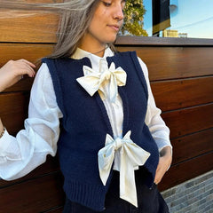 Woman wearing a navy blue vest with white ruffled blouse and decorative bows against a wooden background