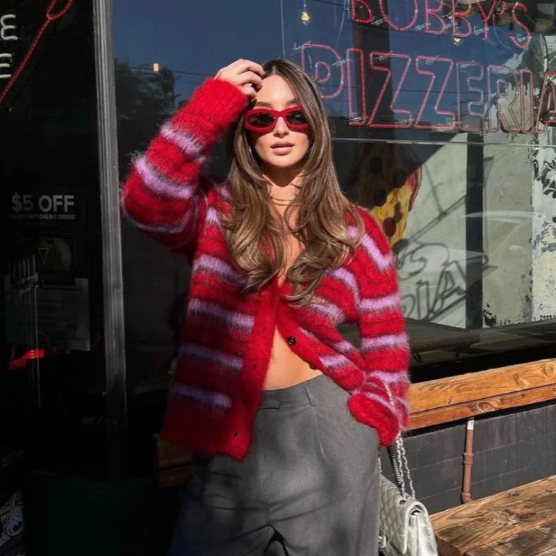 Woman wearing a red striped sweater and sunglasses in front of a pizza shop.